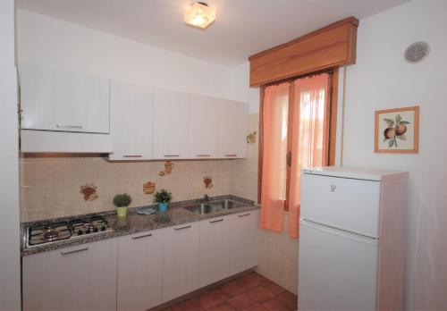 cocina con armarios blancos, fregadero y nevera en Appartamenti Las Palmas, en Lignano Sabbiadoro