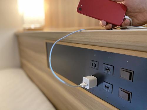 a person holding a cell phone plugged into an electrical outlet at Santiago Hotel in Hiroshima