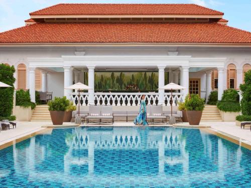 a woman walks by a swimming pool in front of a house at Raffles Singapore in Singapore