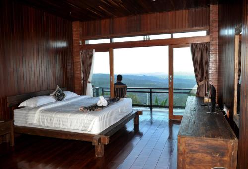 Un hombre sentado en un dormitorio con una cama y una ventana. en Bali Jegeg Munduk Hotel, Bar, and Restaurant, en Munduk