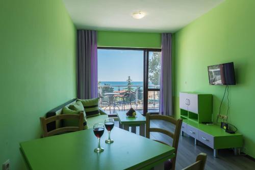 1-st Line Izvora Sea View Apartments on Golden Sands في غولدن ساندز: غرفة معيشة مع طاولة وكأسين من النبيذ