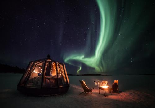 a tent and chairs in the snow under the northern lights at Arctic Lake Experience Oulujärvi Igloos in Kajaani