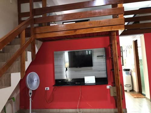 a loft bed with a flat screen tv on a red wall at Apartamento no Centro de Mongaguá in Mongaguá