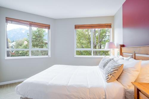 a bedroom with a white bed with two windows at Deer Lodge by Outpost Whistler in Whistler