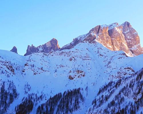 a mountain covered in snow with the sun shining on it at Il Cirmolo delle Saline in Falcade