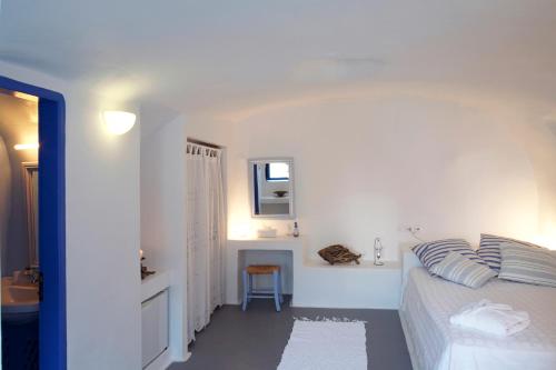 a white bedroom with a bed and a chair at Aghios Artemios Traditional Houses in Imerovigli