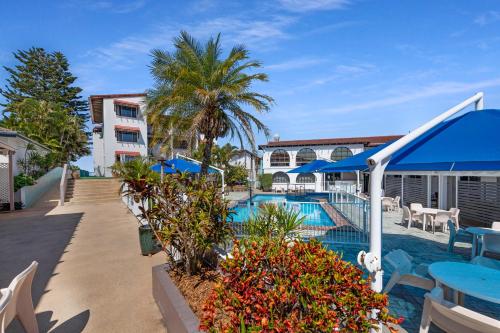 a resort swimming pool with tables and umbrellas at Don Pancho Beach Resort in Bargara