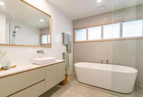 a bathroom with a tub and a sink and a mirror at 22 South - Lennox Head in Lennox Head