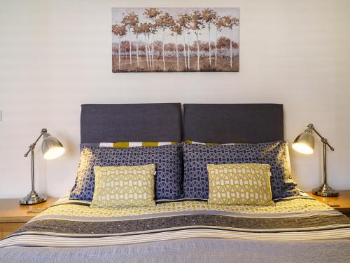 a bed with blue and yellow pillows and two lamps at 2 Brocklehurst Cottages in Buxton