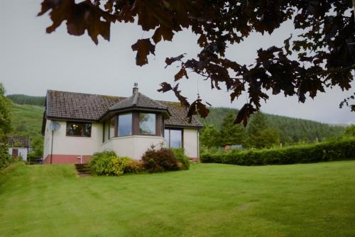 a house on a grassy field with a tree at Maybank in Fort William