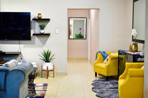 a living room with yellow chairs and a tv at Valleyside Executive Apartments in Ezulwini