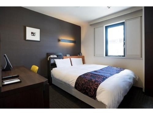 a bedroom with a bed and a desk and a window at Kagoshima Plaza Hotel Tenmonkan - Vacation STAY 97891 in Kagoshima