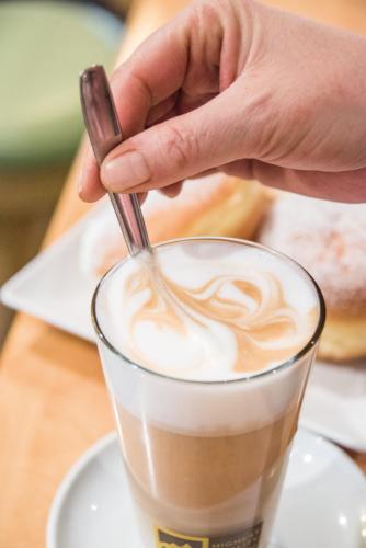 a hand stirring a cup of coffee with a spoon at Apparthotel Feldhof - Living and Bistro in Nova Ponente