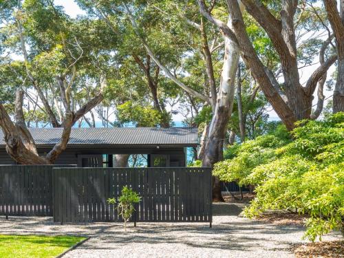 a fence in front of a house with trees at Black Shack on Hyams Beach in Hyams Beach