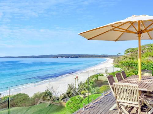 una terraza de madera con sombrilla y playa en Elandra Hyams Beach, en Hyams Beach