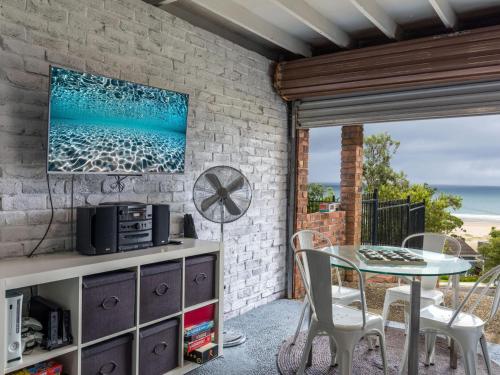 a patio with a table and chairs and a tv on a brick wall at Jewel of Gerroa Gerroa in Gerroa