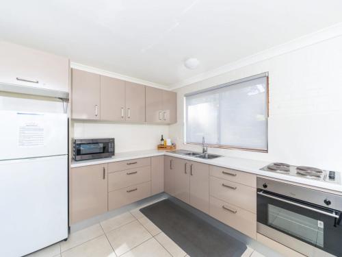 a kitchen with white cabinets and a window and a sink at Sandals at the Bay Downstairs Hyams Beach in Hyams Beach