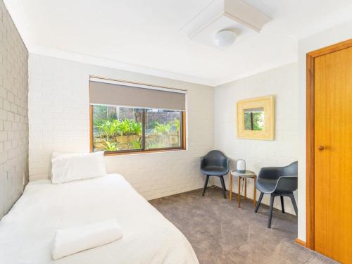a bedroom with a bed and two chairs and a window at Sandals at the Bay Downstairs Hyams Beach in Hyams Beach