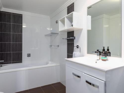 ein Badezimmer mit einem Waschbecken, einer Badewanne und einem Spiegel in der Unterkunft Sebel Harbourside 301 Kiama in Kiama