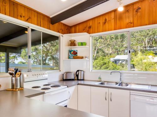 a kitchen with white appliances and two windows at Shanti at Hyams Beach in Hyams Beach