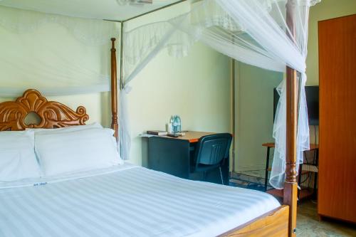 a bedroom with a canopy bed and a desk at Sandton Hotel Kasese in Kasese