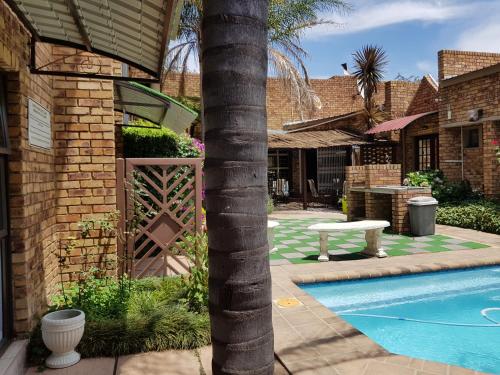 a palm tree next to a house with a swimming pool at Dormio Manor Guest Lodge in Secunda