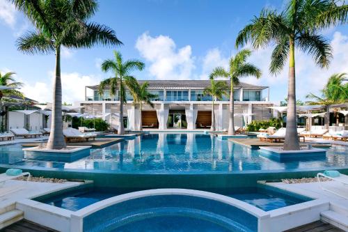 a swimming pool with palm trees in front of a building at Wymara Resort & Villas in Grace Bay