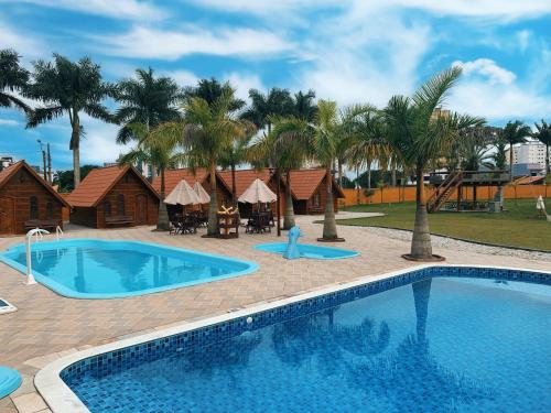 a large swimming pool with palm trees and houses at Chalé Caiçara in Caraguatatuba