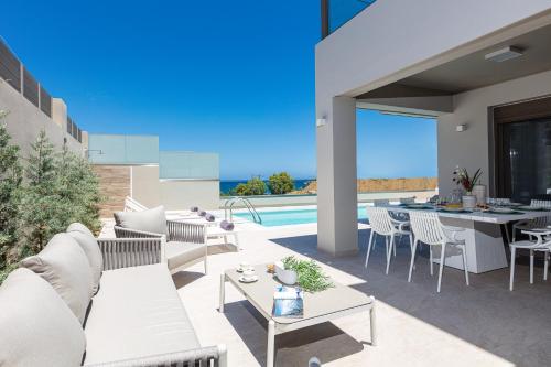 a patio with white furniture and a pool at Lagoon Seaside Villa, Sumptuous Retreat,By ThinkVilla in Panormos Rethymno