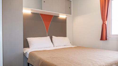 a bed with white pillows and an orange wall at IdeaLazise Camping and Village in Lazise