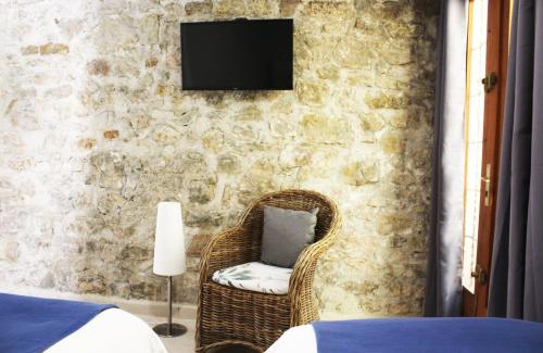 - une chambre avec une chaise en osier et une télévision sur un mur en pierre dans l'établissement Le Mas Des Alizés, à La Colle-sur-Loup