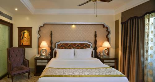 a bedroom with a large bed and two tables and a chair at Indana Palace, Jodhpur in Jodhpur