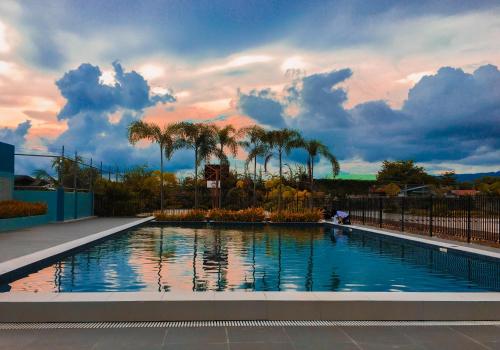 Gibzon's Invitation Suites near Mactan airport في ماكتان: حمام سباحة به أشجار نخيل وسماء غائم