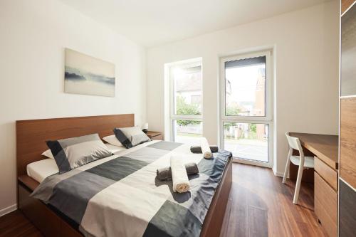Schlafzimmer mit einem großen Bett, einem Schreibtisch und Fenstern in der Unterkunft Ella Apartments in Zlín