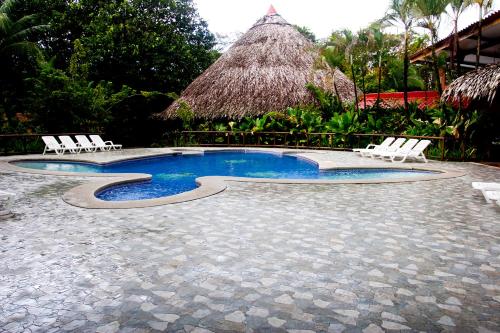 a swimming pool with white chairs and a thatch roof at Turtle Beach Lodge in Tortuguero