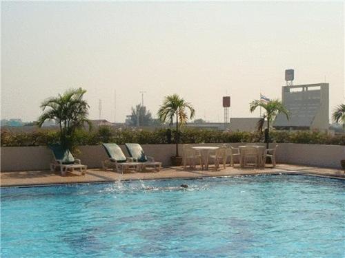 a swimming pool with chairs and a table and palm trees at Charoen Thani Hotel, Khon Kaen in Khon Kaen