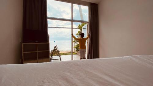 a person looking out of a bedroom window at the ocean at TS Beach House in Phu Quoc