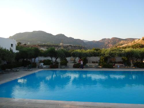 a large blue swimming pool with mountains in the background at Villea Village in Makry Gialos
