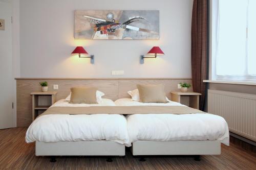2 Betten in einem Schlafzimmer mit 2 Lampen an der Wand in der Unterkunft Ambassador Hotel in De Panne