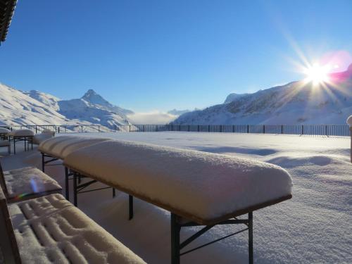 a bench covered in snow with the sun in the background at Hotel Adler in Warth am Arlberg