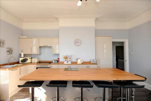eine Küche mit einem Holztisch und einigen Barhockern in der Unterkunft Loveliest Homes Paignton - Wavecrest Apartments - mixed sizes - parking in Paignton