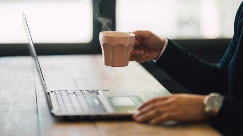 a man holding a cup of coffee in front of a laptop at Hostel ilfaro Kurume in Kurume