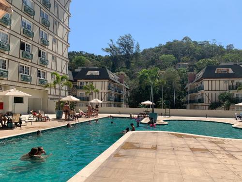 a pool with people in the water next to a building at Flat Manacas Granja Brasil Itaipava in Itaipava