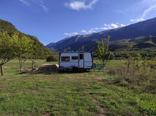 a white trailer parked in a field with mountains at Albturist Ecocamping Përmet & Outdoor Sports Center in Përmet