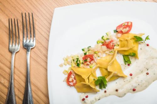 a white plate with food on a table with two forks at Hotel Castel Oswald von Wolkenstein in Castelrotto