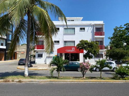 a white building with a red awning and palm trees at Hotel LB in Manzanillo