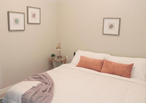 a white bed with an orange pillow on it at Sleepover Premier Downtown Des Moines Apartments in Des Moines