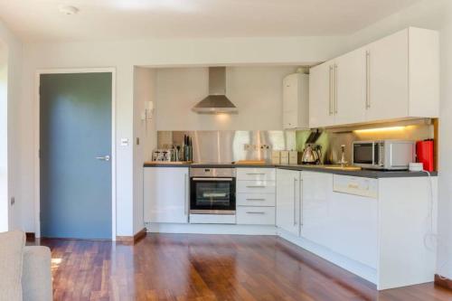 a kitchen with white cabinets and a wooden floor at Luxury Summerhouse Annexe in lush gardens in Fowey in Fowey