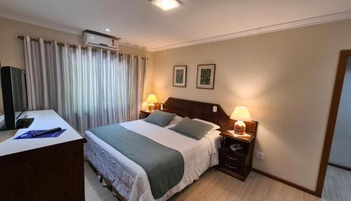 a bedroom with a bed and two lamps and a television at Hotel Azaleia in Gramado