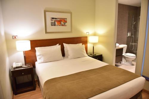 a bedroom with a bed with two lamps and a bathroom at Lastarria Hotel & Aparts in Santiago